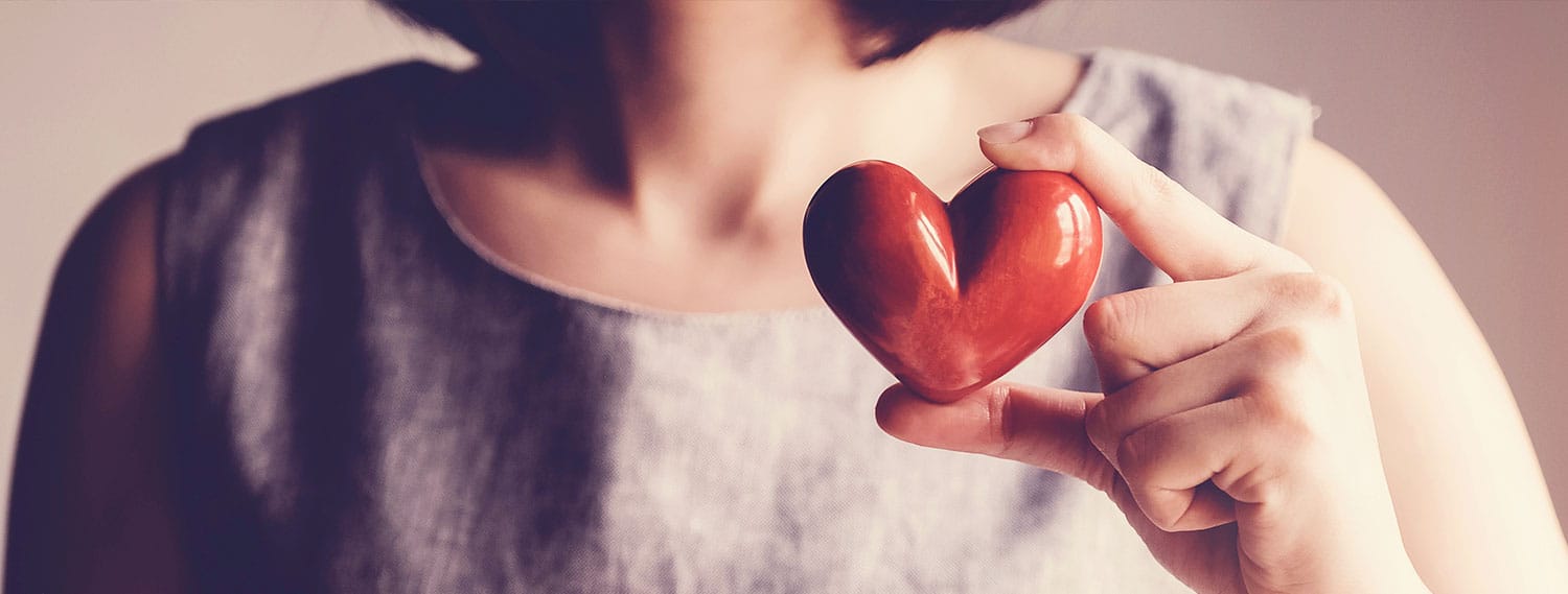 Was hilft bei Bluthochdruck Banner. Frau hält ein Herz aus Holz