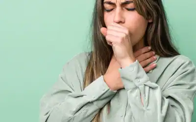 Frau mit Bronchitis hält sich Faust vor den Mund beim Husten und greift sich an den Hals