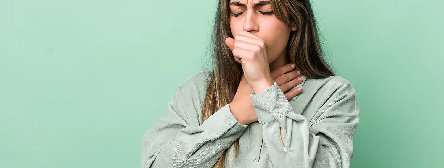 Frau mit Bronchitis hält sich Faust vor den Mund beim Husten und greift sich an den Hals
