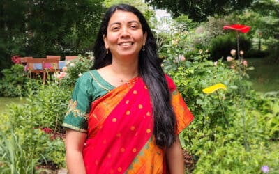 Dr. Sharmili Madishetty in rotem Sari mit grüner Bluse im sommerlichen Garten – Ayurveda-Ärztin bei RoSana
