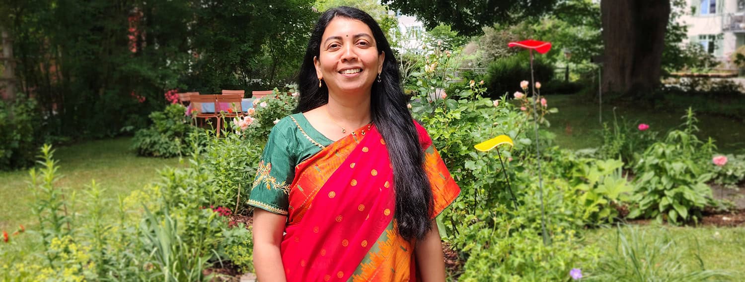 Dr-Sharmili-Madishetty-Ayurveda-im-Sommer Dr. Sharmili Madishetty in rotem Sari mit grüner Bluse im sommerlichen Garten – Ayurveda-Ärztin bei RoSana