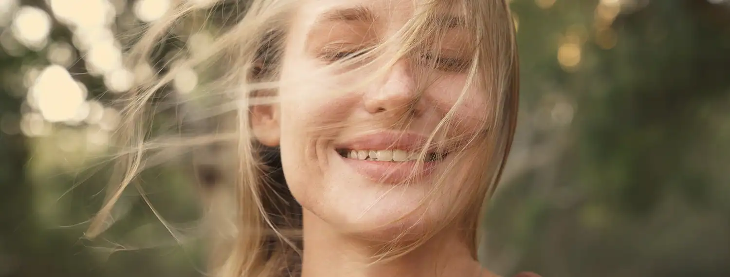 Sitkari Pranayama Lächelnde Frau mit im Wind wehenden Haaren praktiziert Sitkari Pranayama im Freien