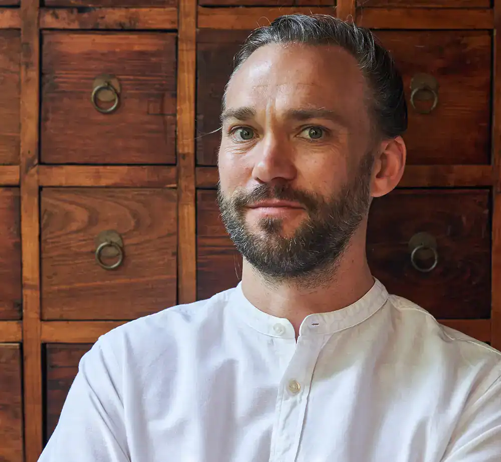 Simon Mayier, Ayurveda-Koch bei RoSana, Autor des Prana-Kochbuchs, portrait vor Holzschubladen