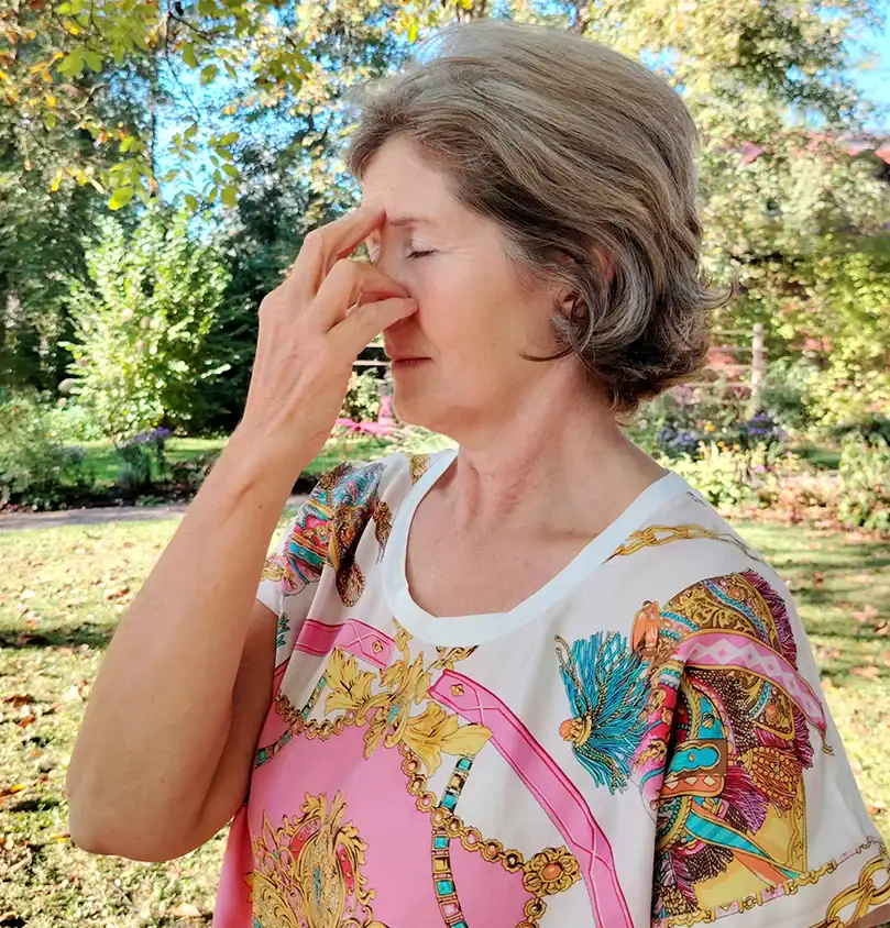 Frau mit kurzen Haaren übt Nadi Shodhana im Garten: Wechselatmung mit geschlossenen Augen, RoSana Ayurveda Kurzentrum
