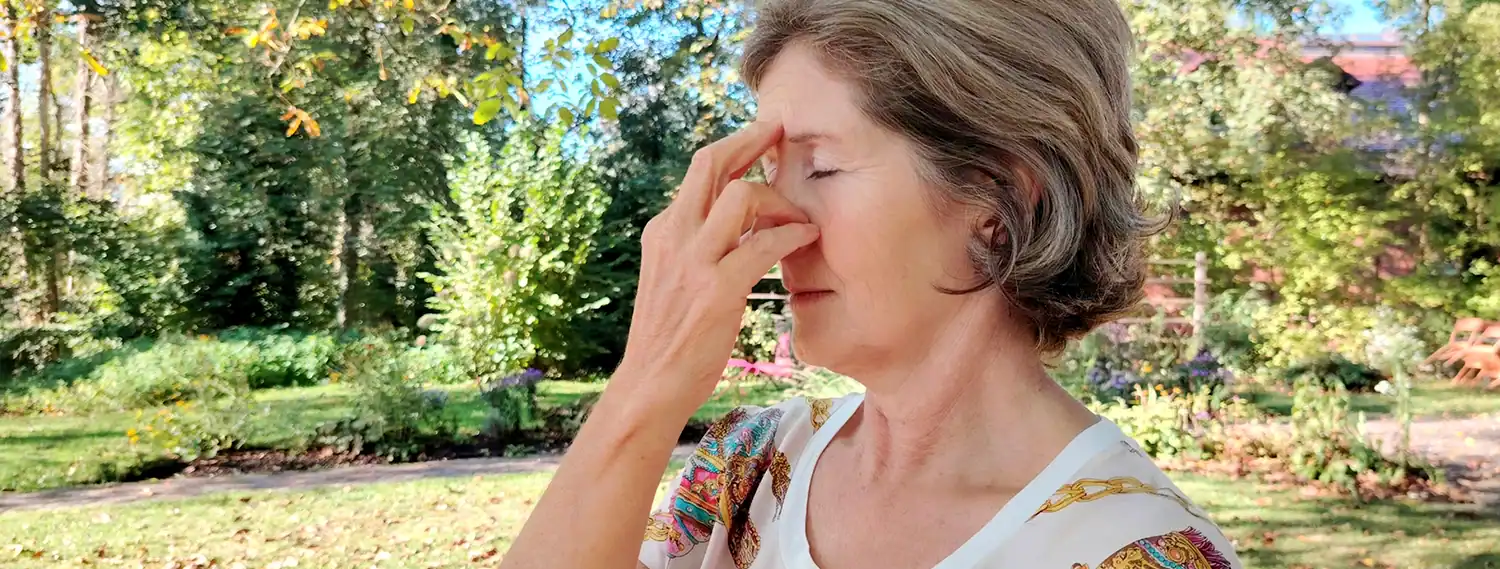 Ältere Frau übt Nadhi Shodhana Atmung im Garten, Finger an der Nase – Pranayama bei RoSana Ayurveda Kurzentrum